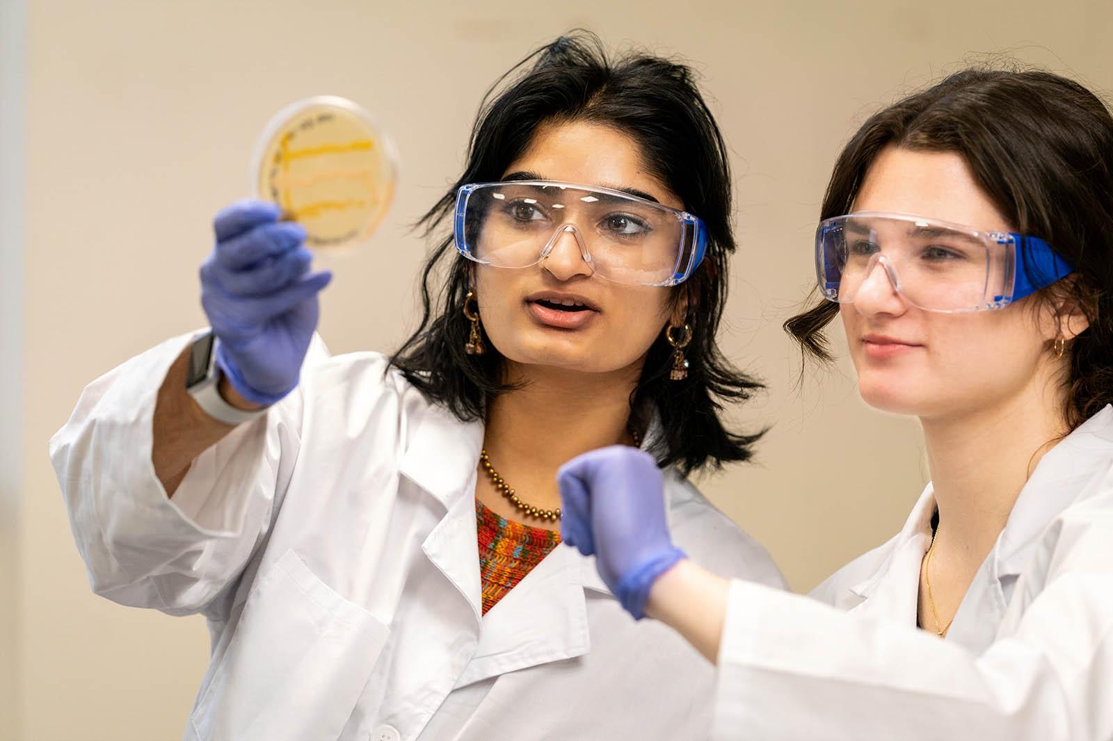 Two students in protective lab gear work on a science experiment together